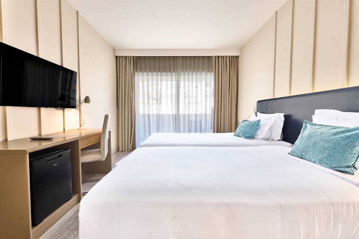 Una habitación de hotel con una cama, un escritorio con televisor y una ventana con cortinas.