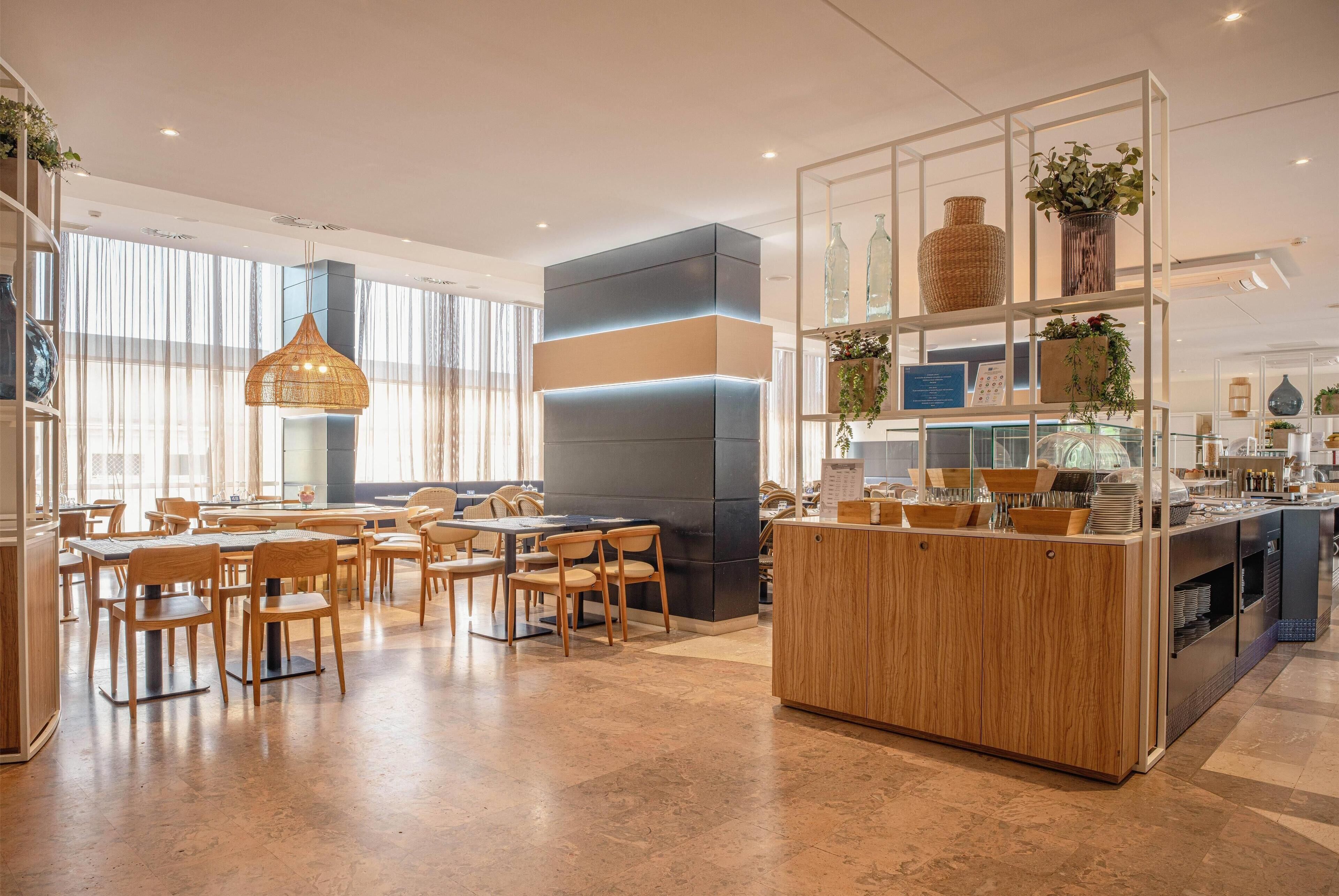 A modern restaurant with wooden tables and chairs, a central counter, and a display of vases and plants.