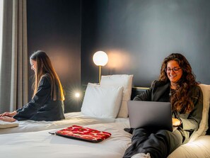Een hotelkamer met twee bedden, een bedlampje en een laptop op een van de bedden.
