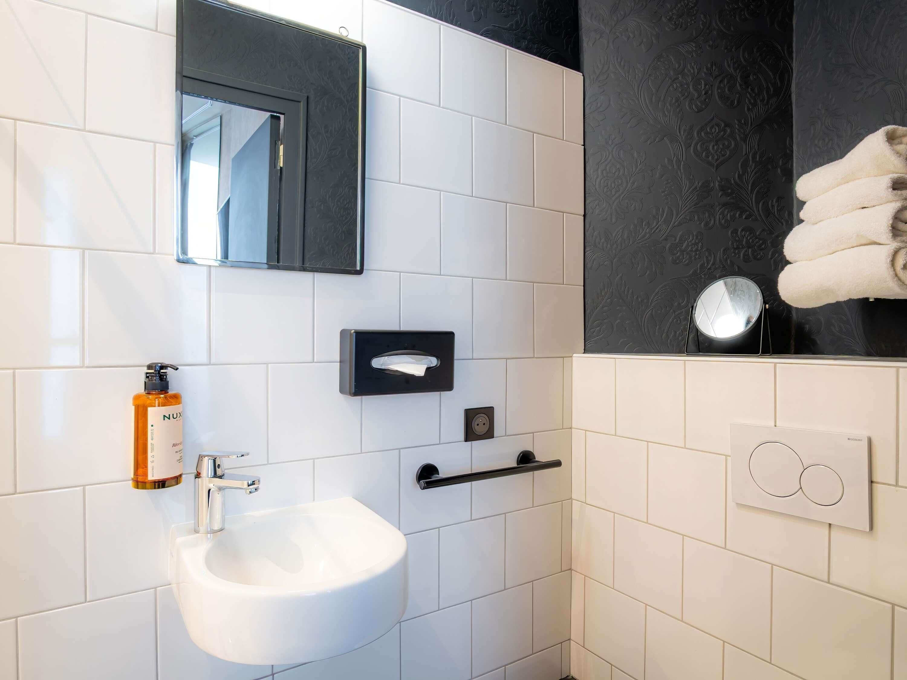 A modern bathroom with a white sink, a mirror, a towel rack, and a soap dispenser.