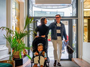 Entrada de hotel con un cochecito de bebé, un niño y un adulto caminando.