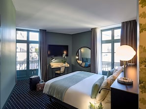 Una camera d'albergo con un letto, una scrivania con una sedia, una televisione, uno specchio e una finestra con tende.