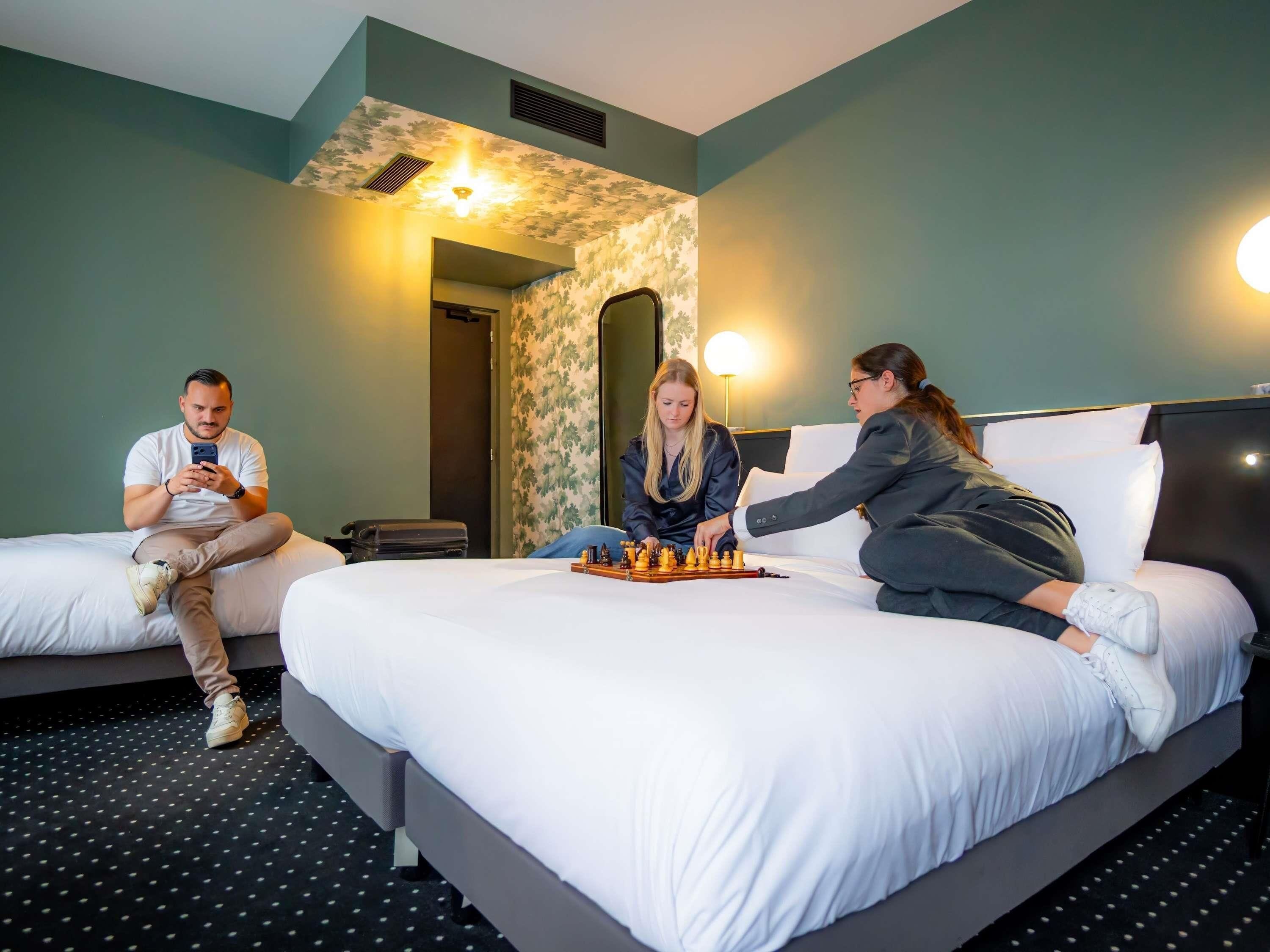A hotel room with a large bed, a chessboard, and a person playing chess.