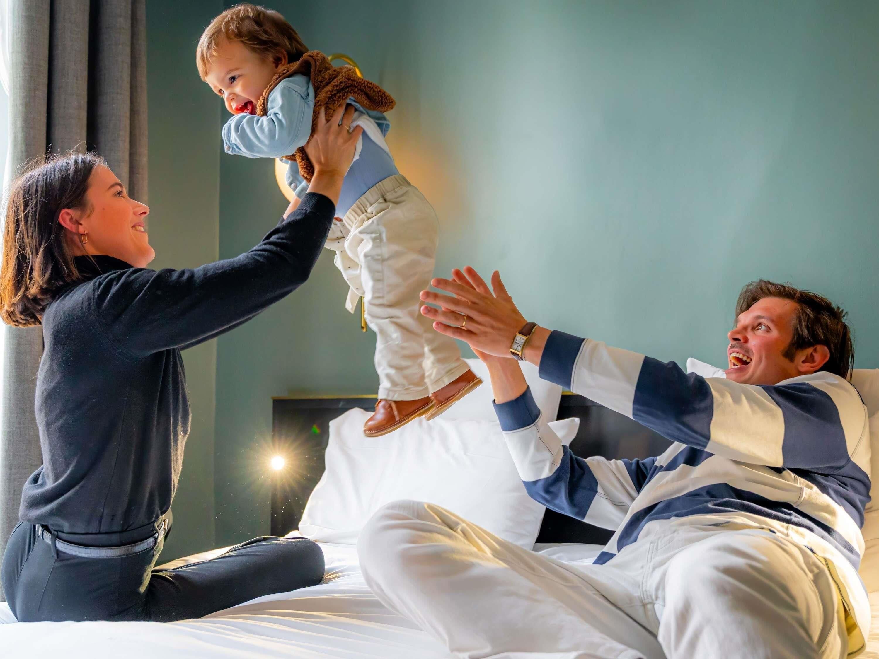 A person sitting on a bed with a child being held up by another person.