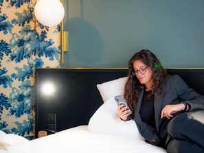 Una persona sentada en una cama en una habitación con papel tapiz estampado y un cabecero moderno.