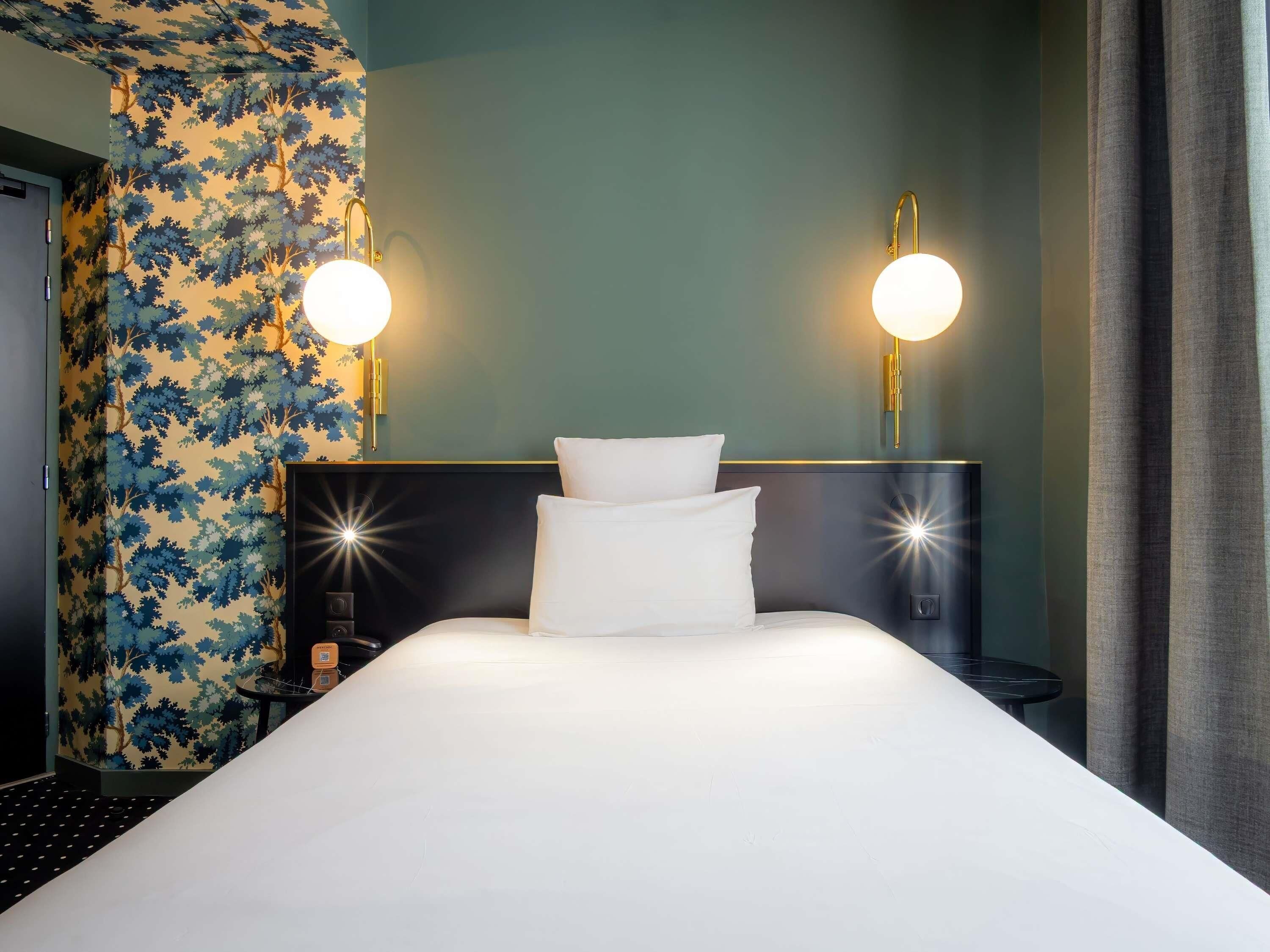 Une chambre d’hôtel avec un grand lit, deux lampes de chevet, un mur orné d’un motif de feuilles et une tête de lit sombre.