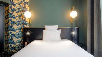 Une chambre d’hôtel avec un grand lit, deux lampes de chevet, un mur orné d’un motif de feuilles et une tête de lit sombre.