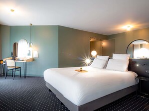 Une chambre d’hôtel avec un grand lit, un bureau avec une chaise, un miroir et une table ronde.