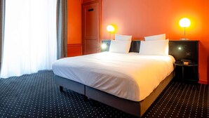 Een hotelkamer met een groot bed, twee nachtkastjes met lampen, een deur en een raam met gordijnen.