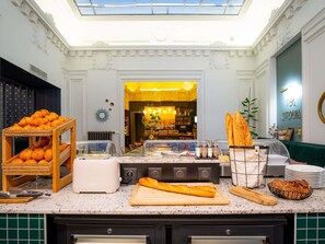 Zona de desayuno buffet con diversos pasteles, pan y una estación de café.