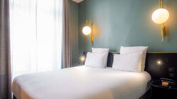 A hotel room with a large bed, two wall-mounted lamps, a bedside table with a lamp, and a window with curtains.