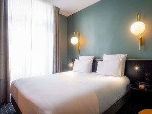 Habitación de hotel con una cama grande, dos lámparas de pared, una mesita de noche con lámpara y una ventana con cortinas.