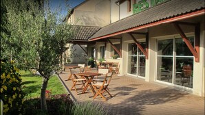 An outdoor patio with wooden tables and chairs, a small garden area, and a building with a sign that reads "RESITAL". - Sure Hotel by Best Western Rennes Chantepie (Chantepie)