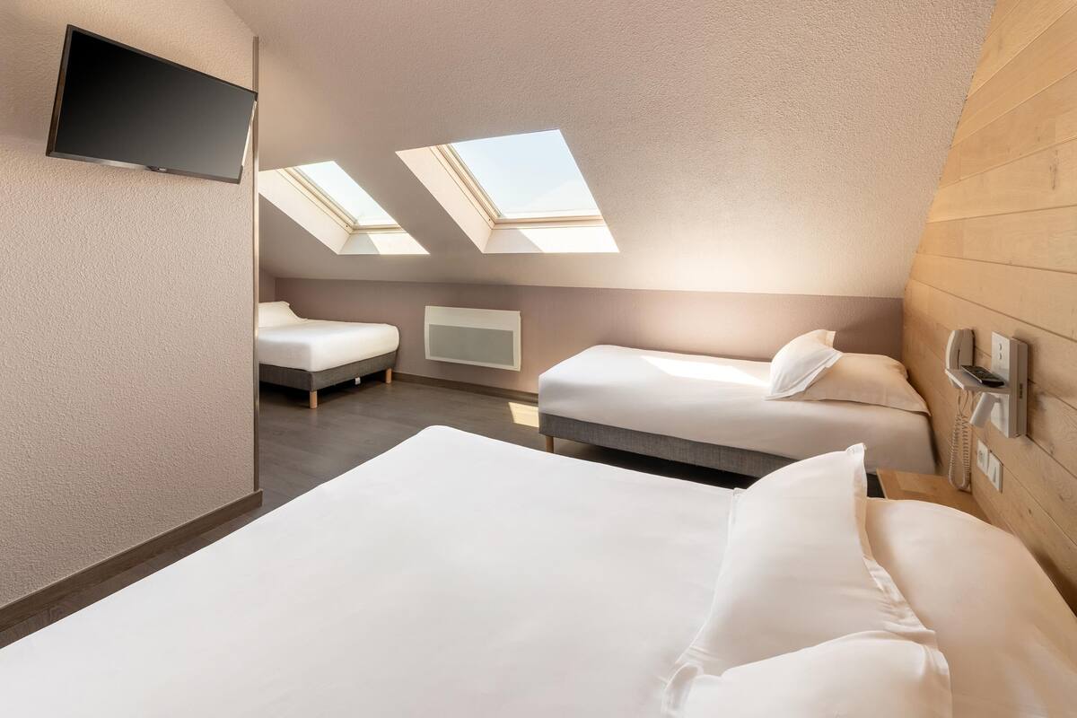 Ein Hotelzimmer mit zwei Betten, einem Flachbildfernseher, einem Telefon und Dachfenstern.