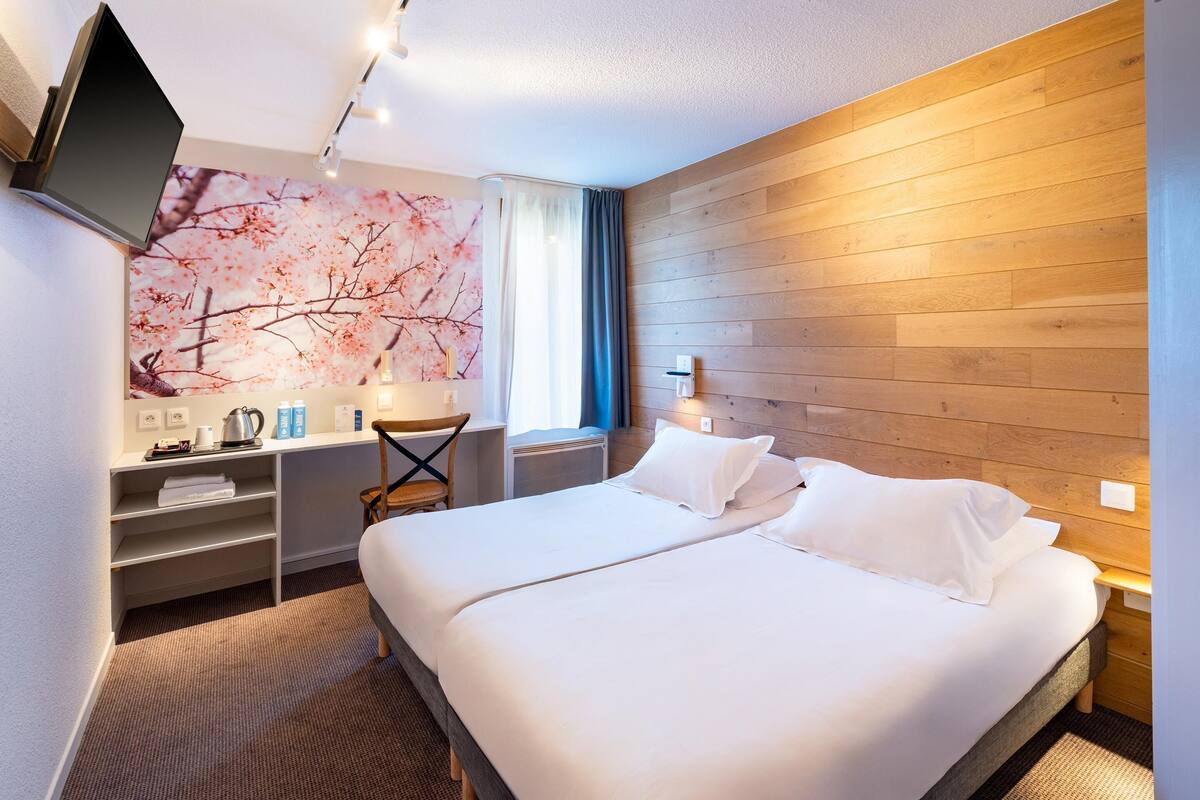 Ein Hotelzimmer mit einem großen Bett, einem Schreibtisch mit Stuhl, einem an der Wand montierten Fernseher und einer Wandverkleidung aus Holz.