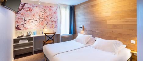 A hotel room with a large bed, a desk with a chair, a TV mounted on the wall, and a wooden panel wall.