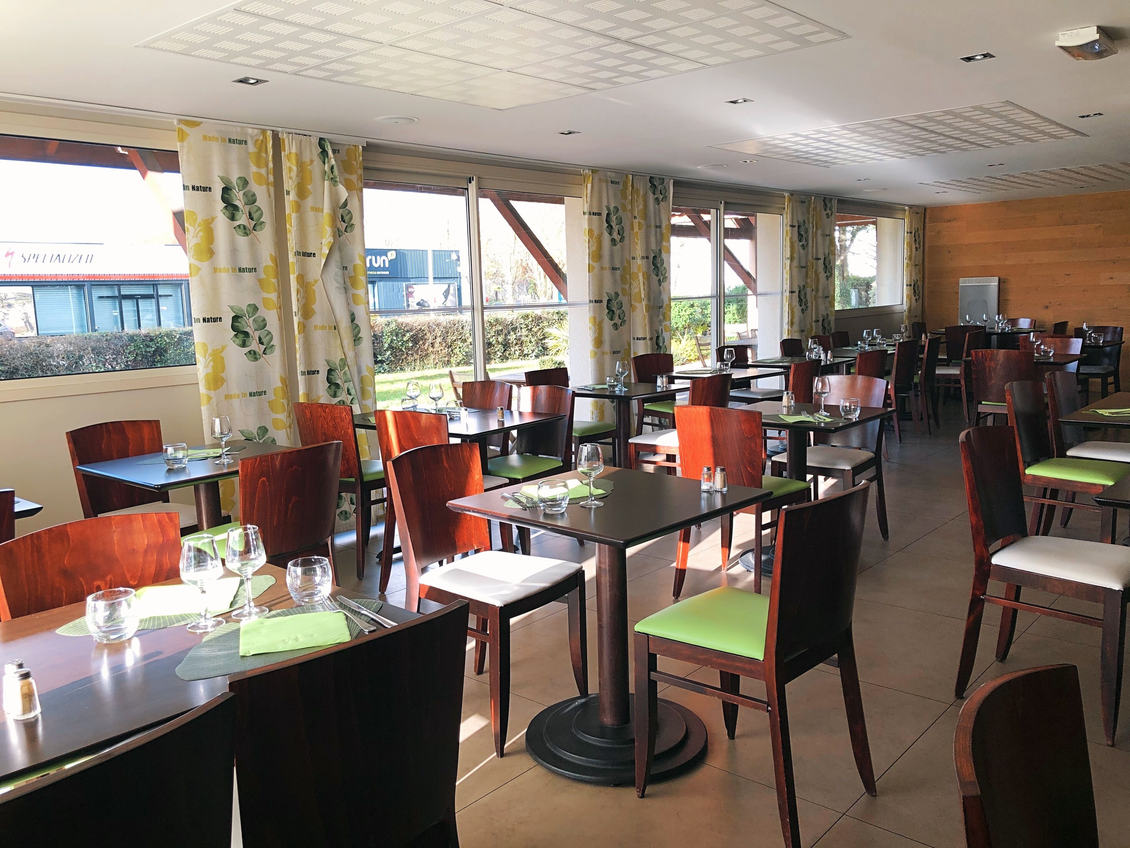 Un restaurante con varias mesas y sillas, ventanas amplias con cortinas y vistas al exterior.