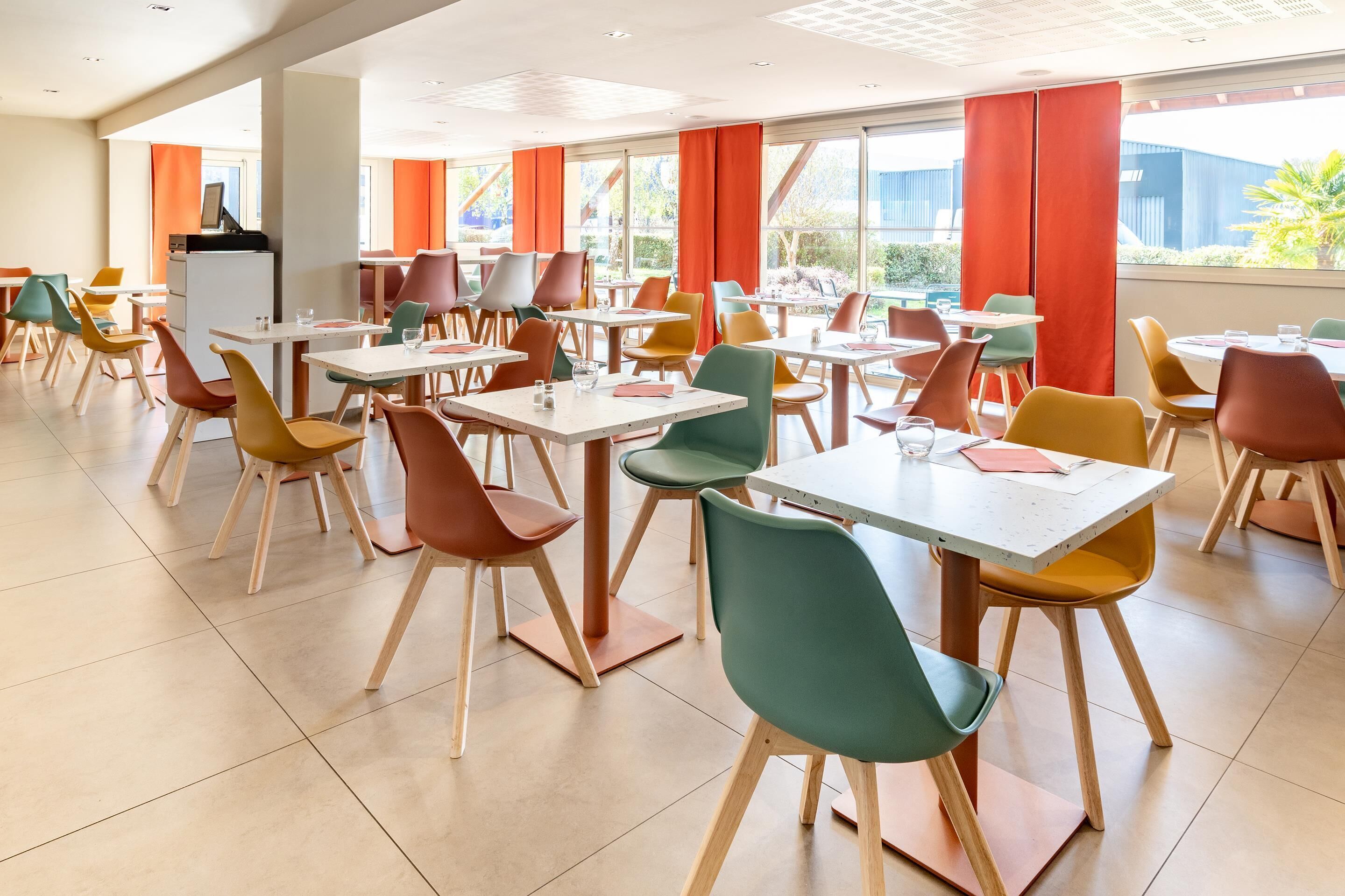 A spacious dining area with multiple tables and chairs, large windows with orange curtains, and a modern interior design.