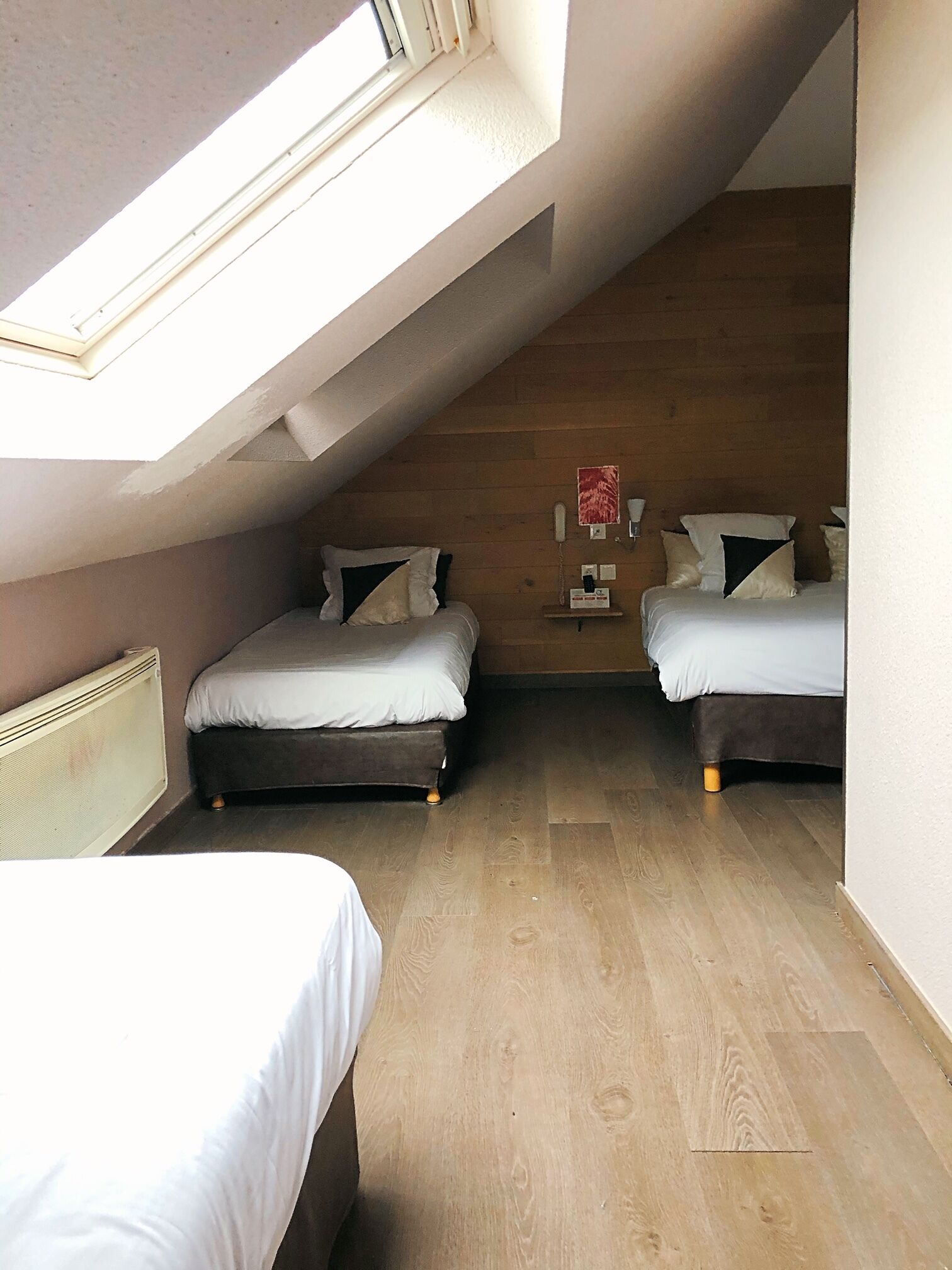 Een klein, knus zolderkamer met twee bedden, een schuine balkenkap en een houten vloer.