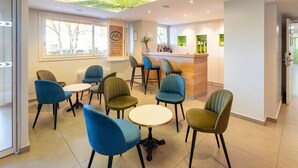 A modern interior with round tables and chairs, a reception desk, and a view of trees through a large window. - Sure Hotel by Best Western Rennes Chantepie (Chantepie)