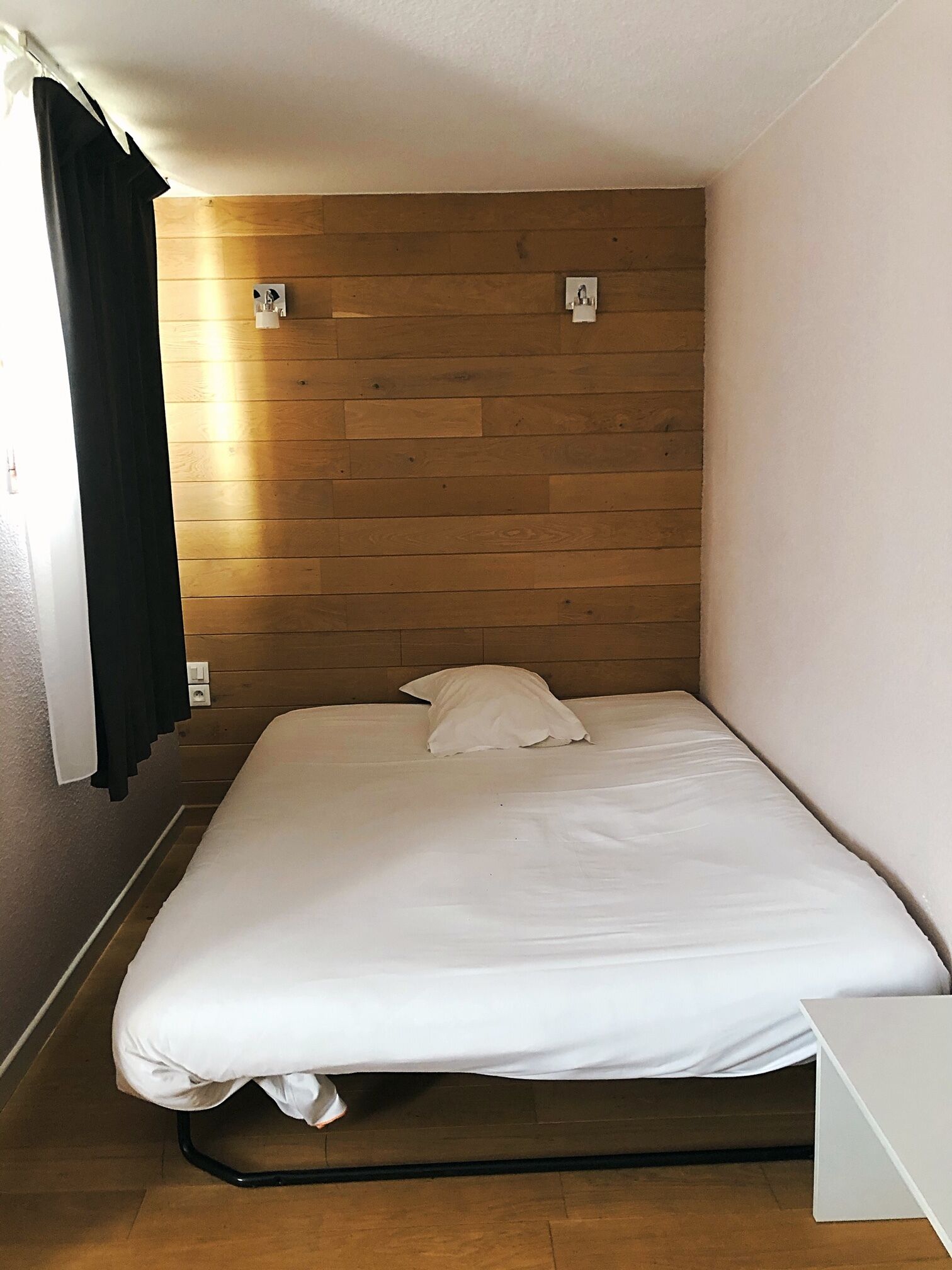 Una cama individual con ropa de cama blanca en una habitación con paneles de madera.