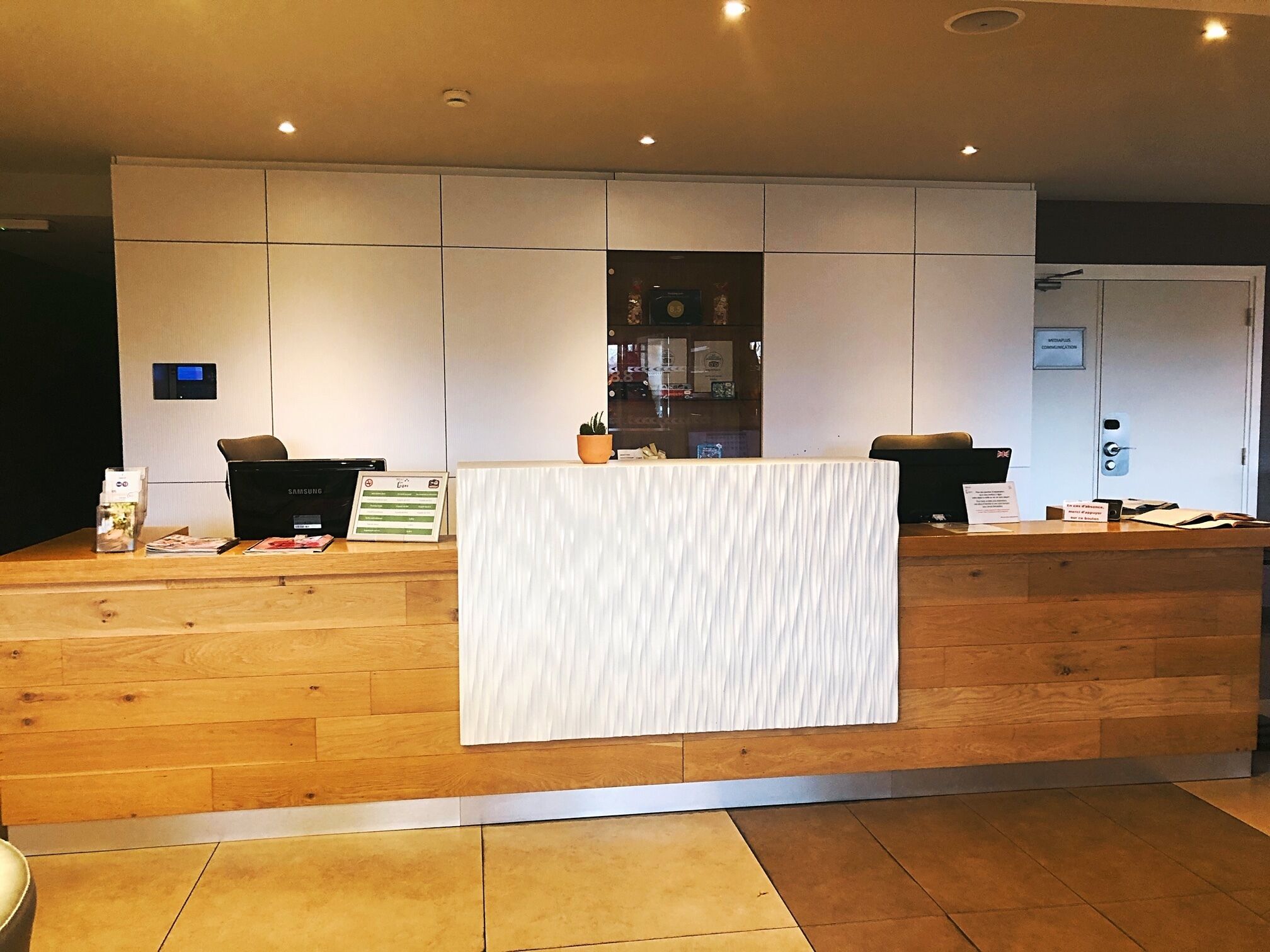 Un mostrador de recepción con un dispositivo Samsung, una planta en maceta y un cartel.
