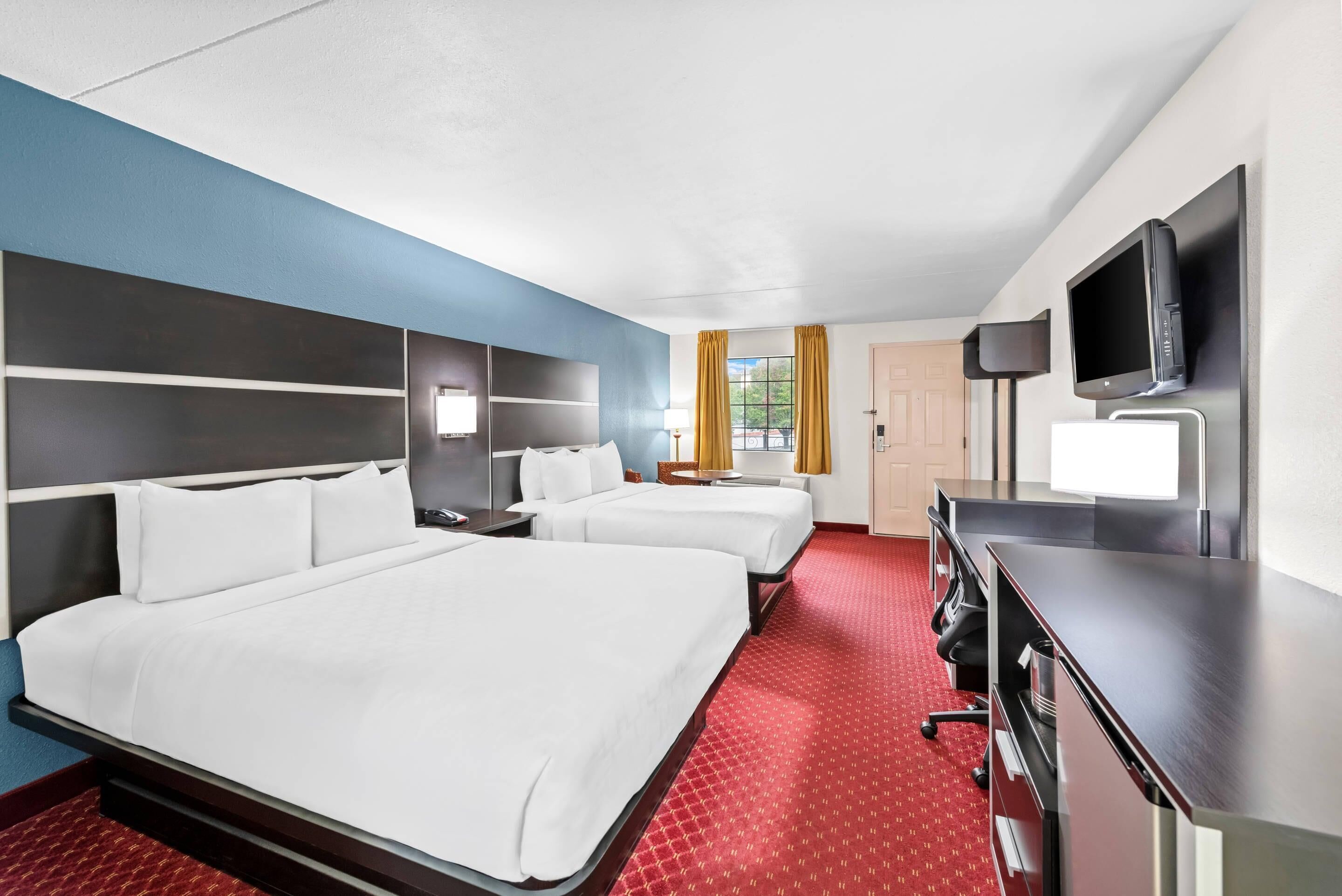 Une chambre d’hôtel avec deux lits, un bureau, un téléviseur à écran plat et une fenêtre avec des rideaux.