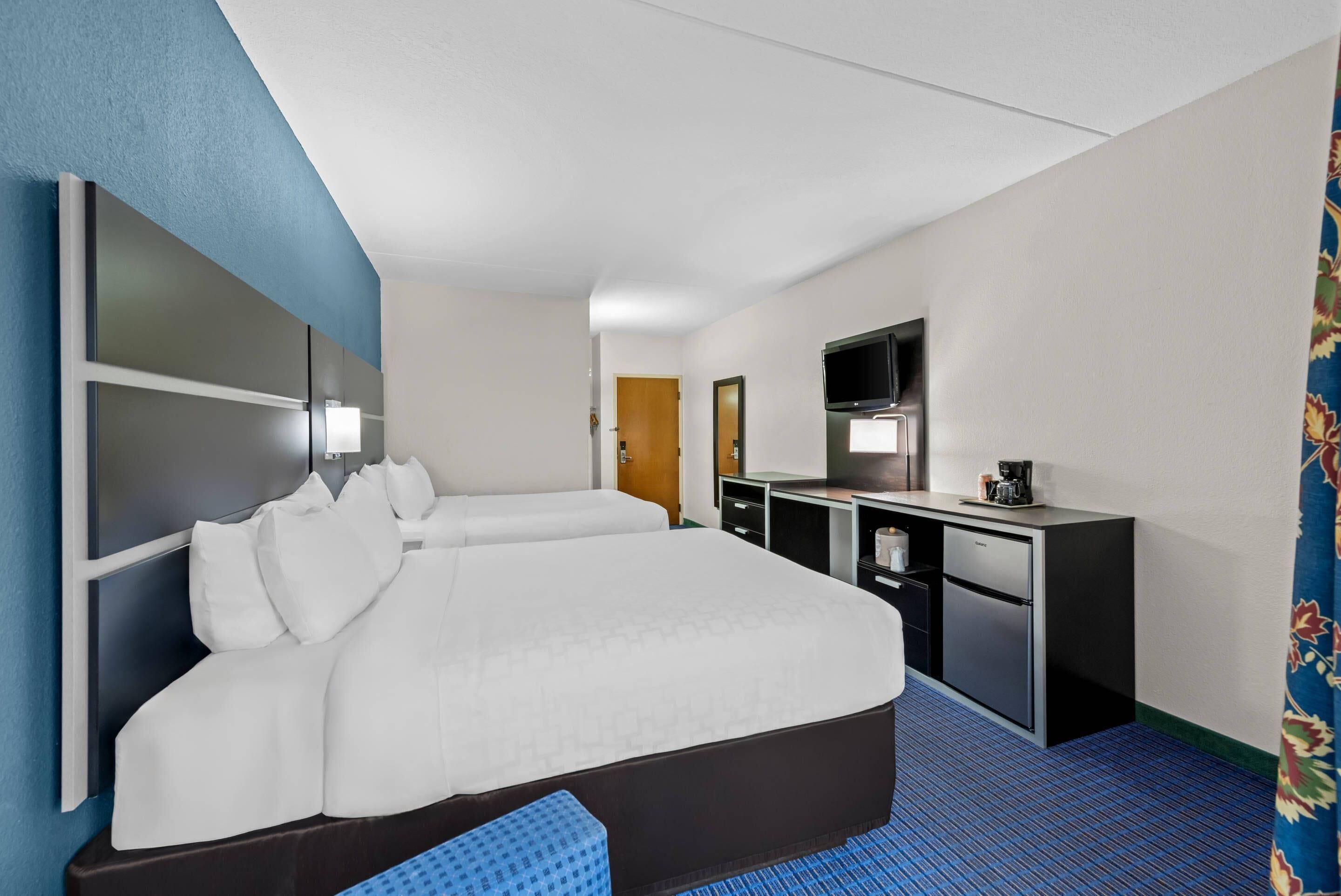 A hotel room with a large bed, a desk, a television, and a minibar.