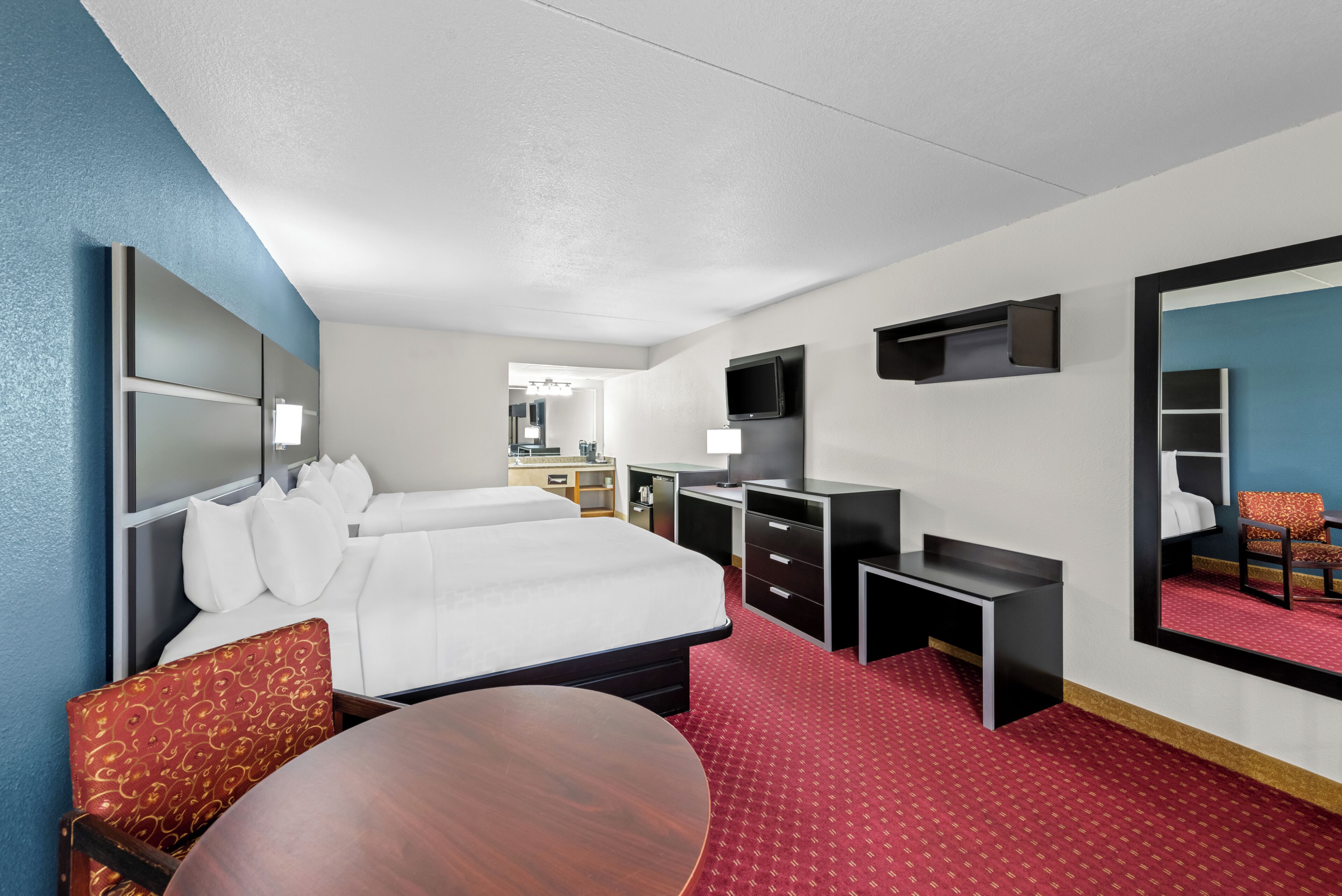 A hotel room with a bed, desk, chair, TV, and a mirror.