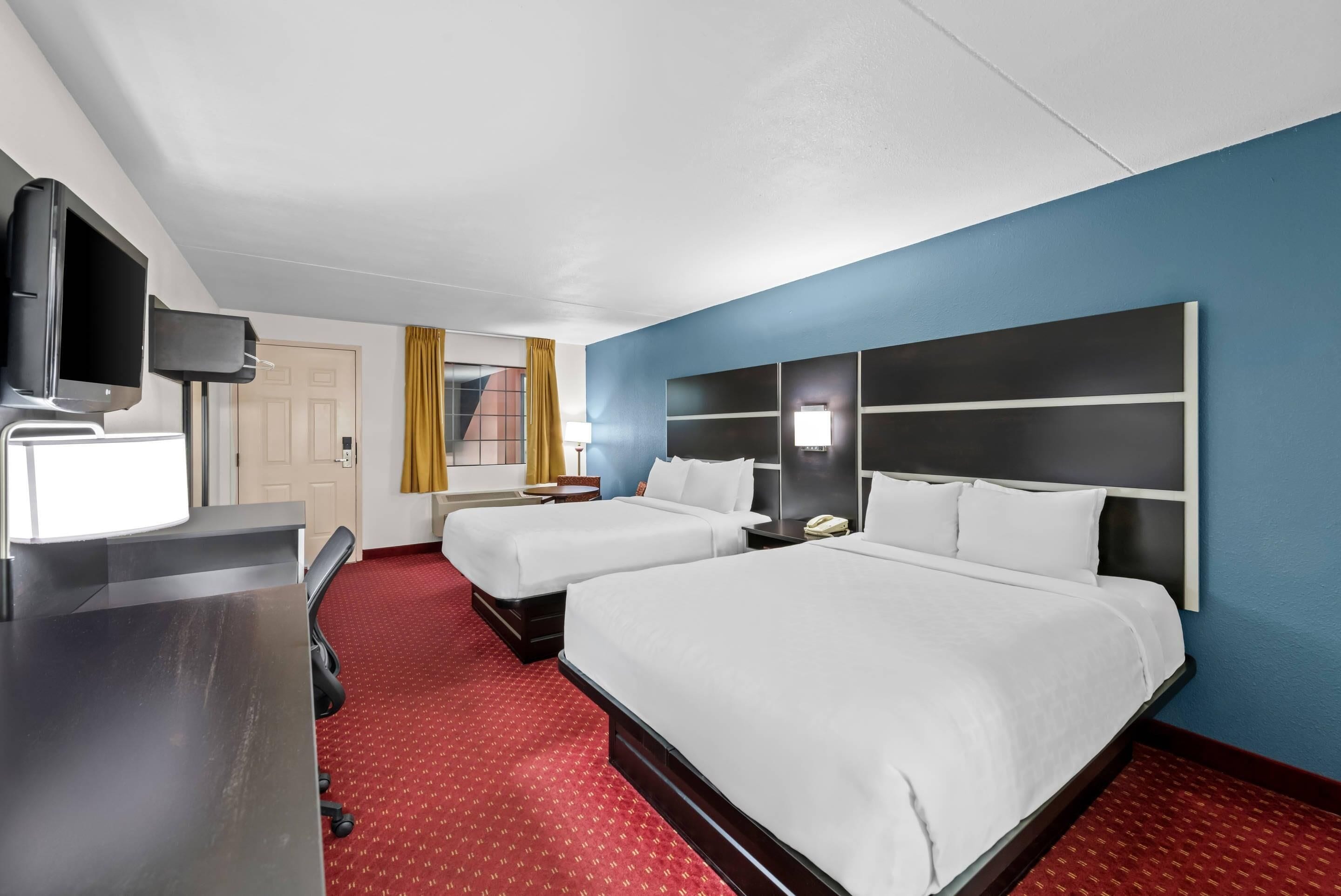 Ein Hotelzimmer mit zwei Betten, einem Schreibtisch und einem Fernseher, sowie einem roten Teppich.