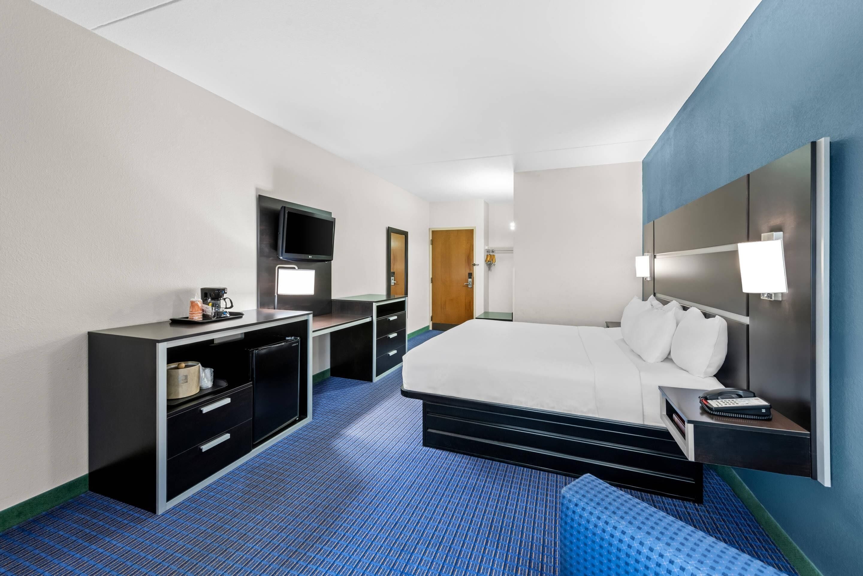 Ein Hotelzimmer mit einem Bett, einem Schreibtisch mit Fernseher, einem Kleiderschrank und einem Nachttisch mit Lampe.