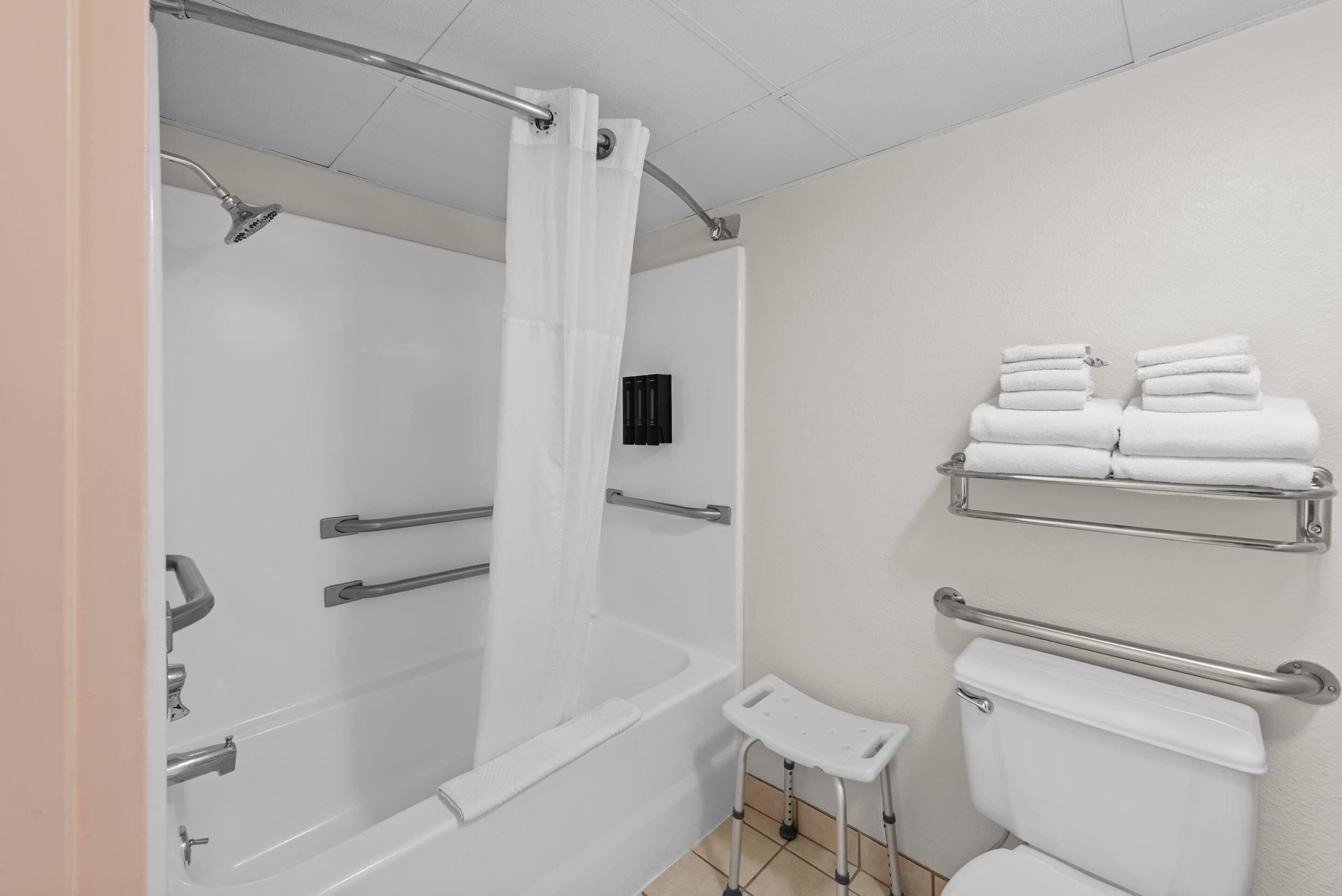A bathroom with a bathtub, shower, toilet, and handrails.