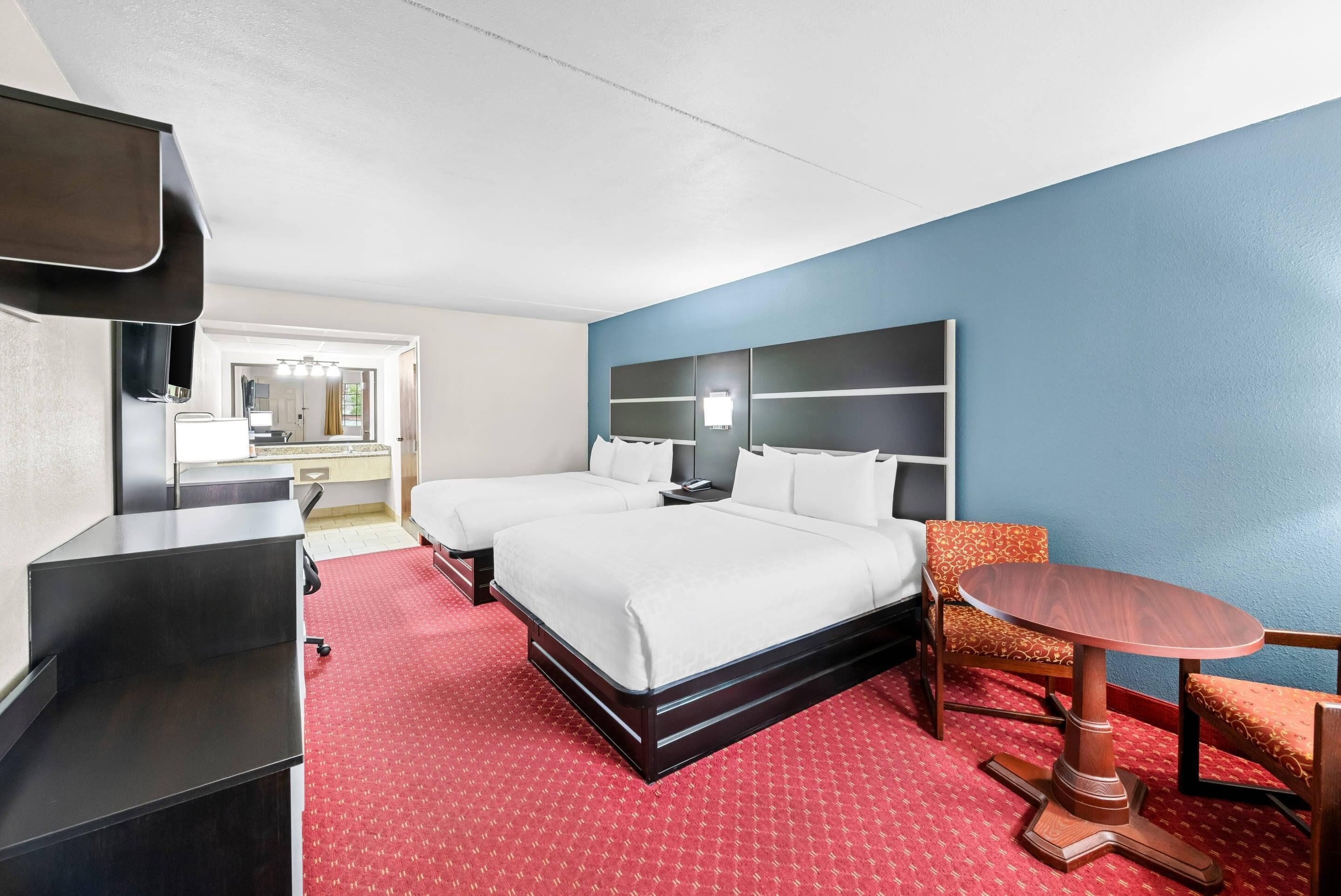 A hotel room with a bed, a desk, a chair, a small table, and a TV.