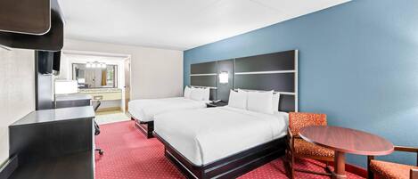 A hotel room with a bed, a desk, a chair, a small table, and a TV.