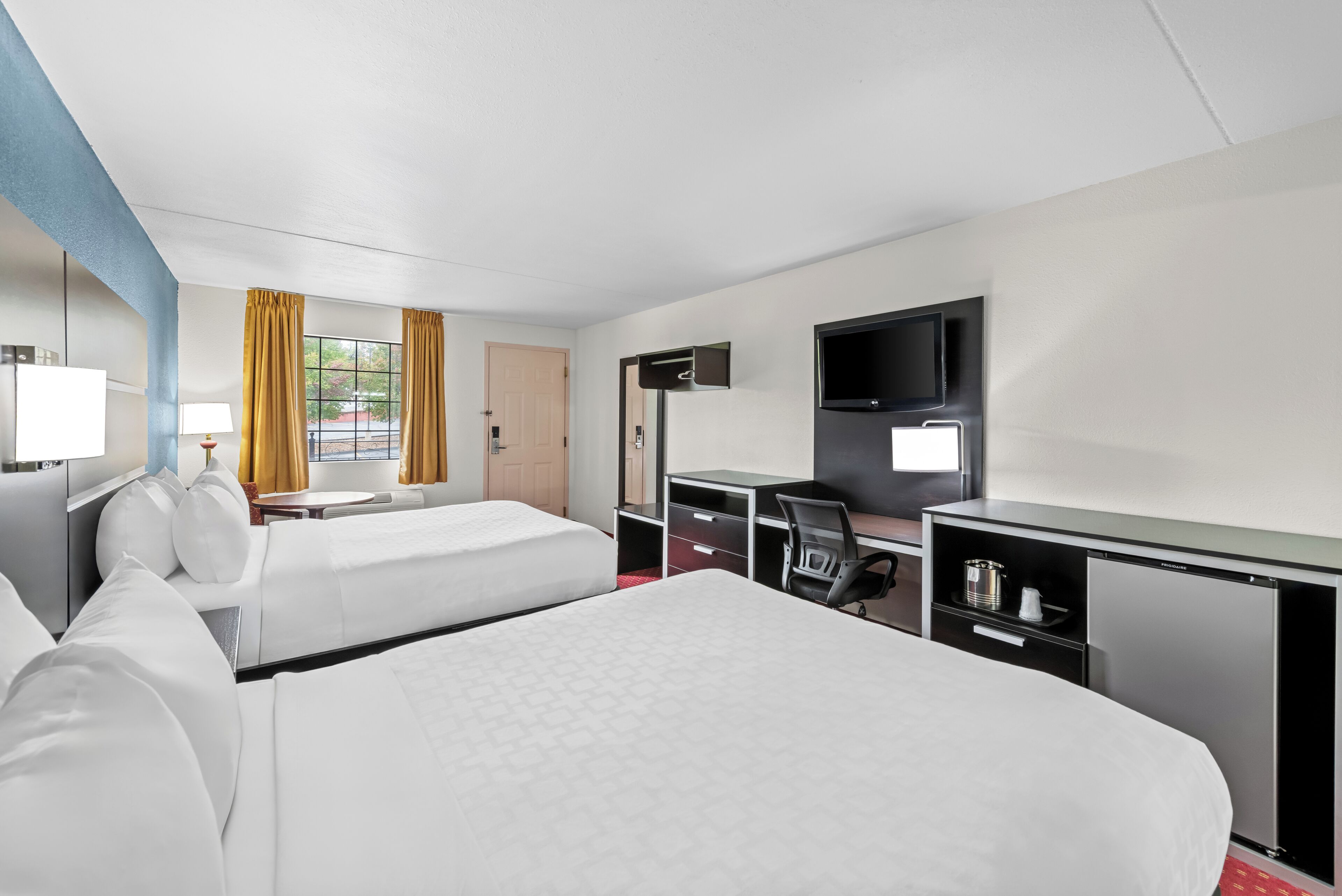 Habitación de hotel con dos camas, un escritorio, una silla, un televisor y un minibar.