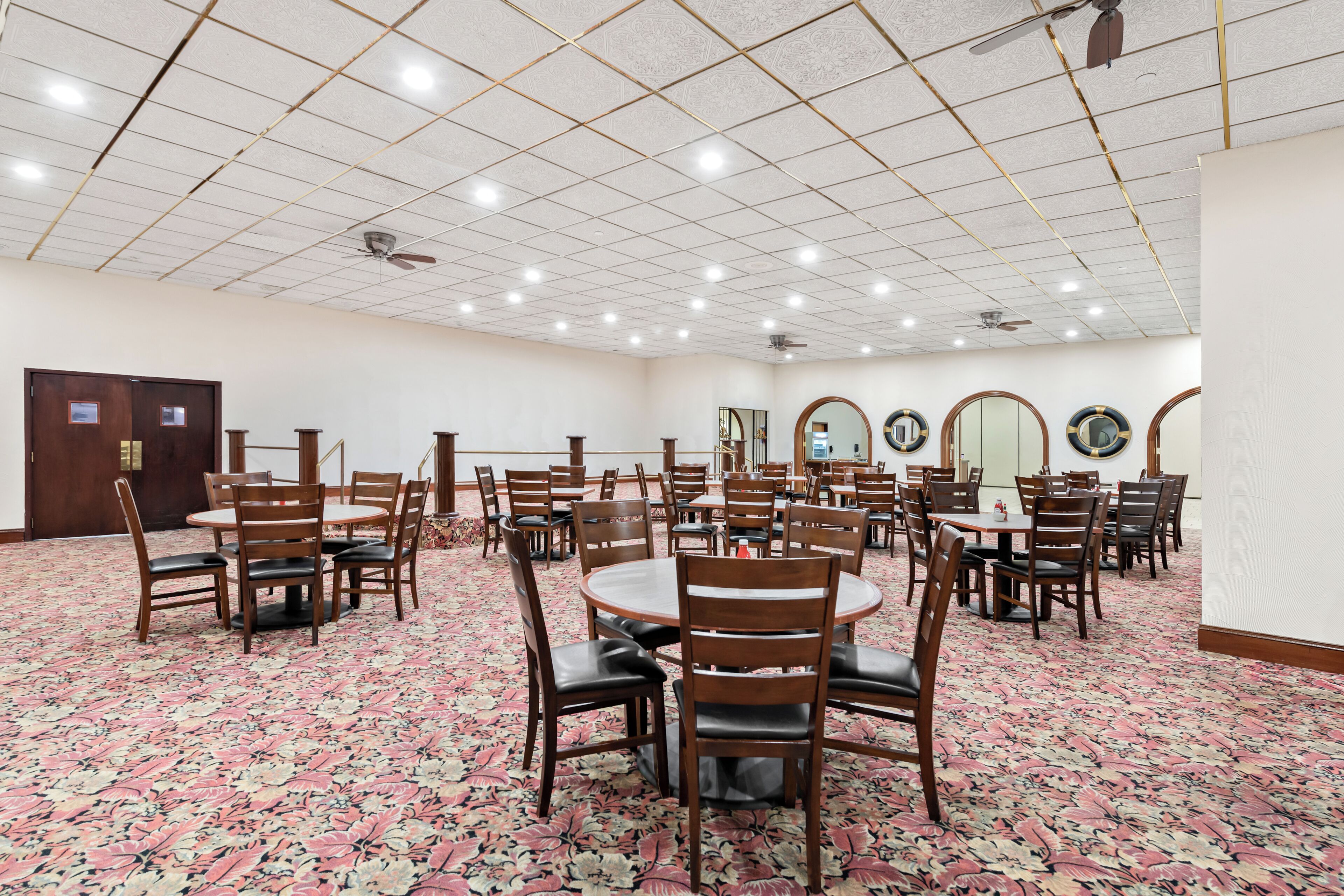 A conference room with multiple tables and chairs, a patterned carpet, and ceiling lights.