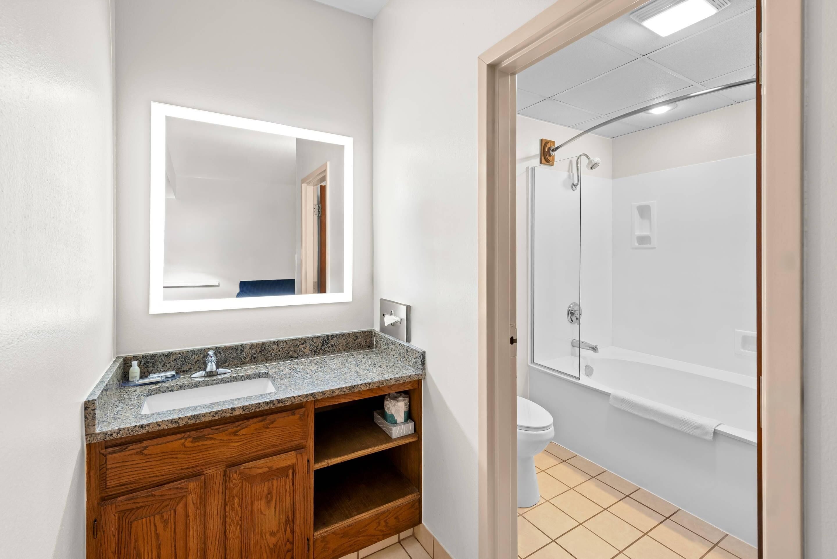 A bathroom with a granite countertop sink, wooden vanity, a mirror, a toilet, and a glass-enclosed shower.