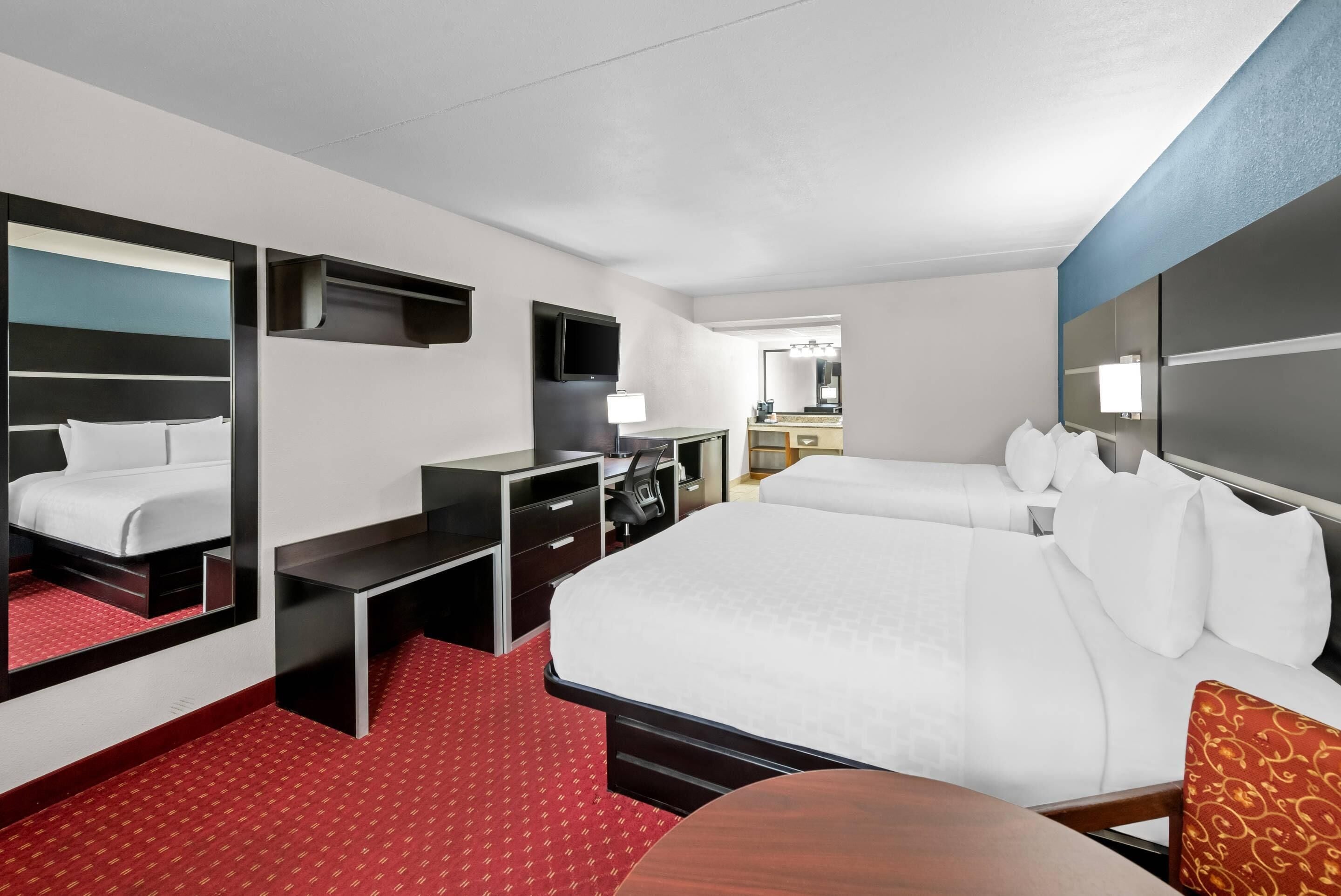 A hotel room with a large bed, a desk, a chair, a TV, and a mirror.