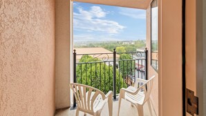Un balcón con dos sillas blancas y vistas a un paisaje verde y edificios.