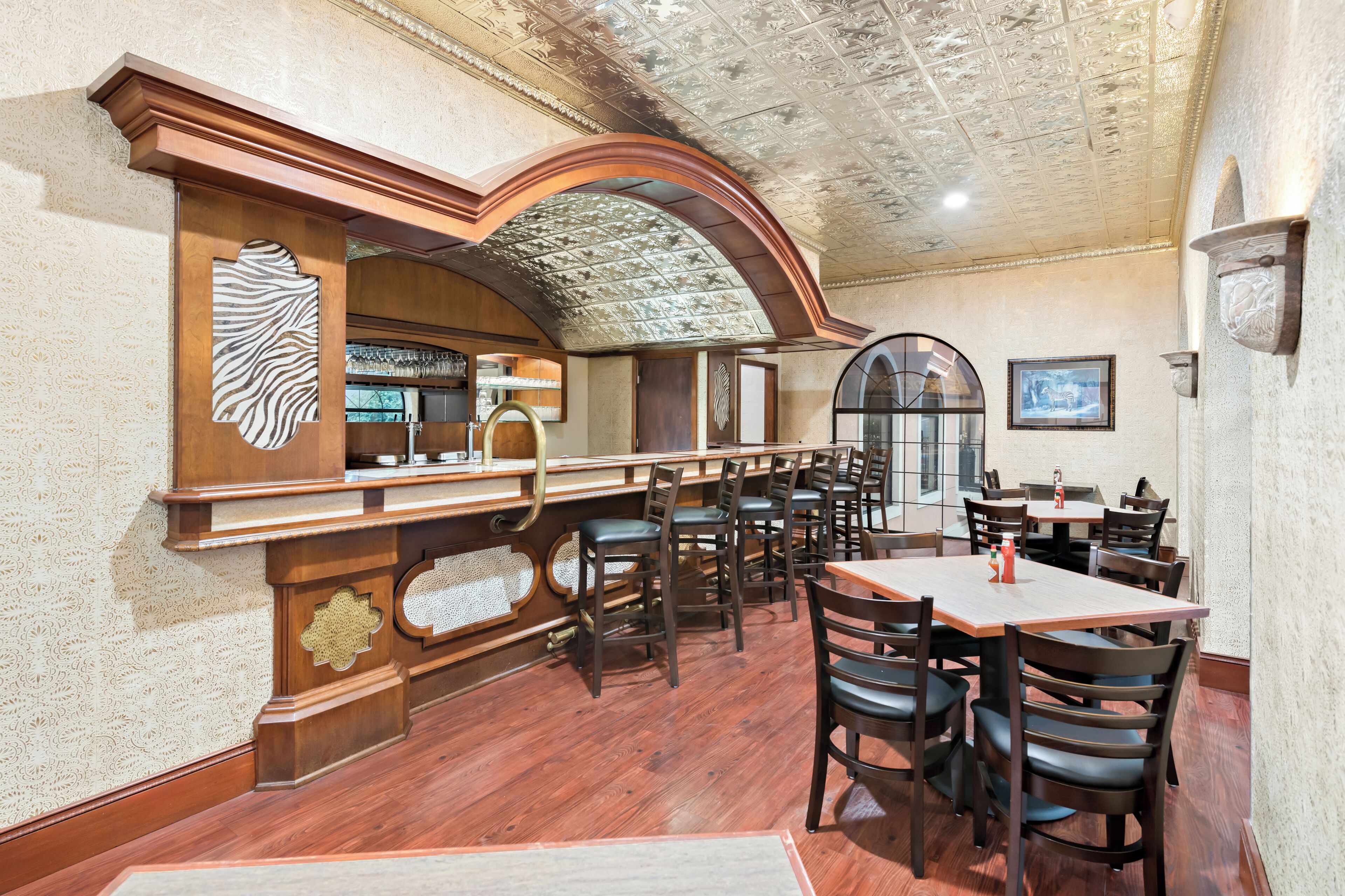 Un restaurant doté d’un bar, de chaises en bois et d’un plafond orné de motifs.