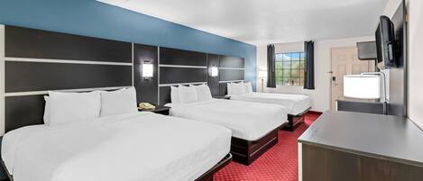 A hotel room with three beds, a desk, a TV, and a window with curtains.