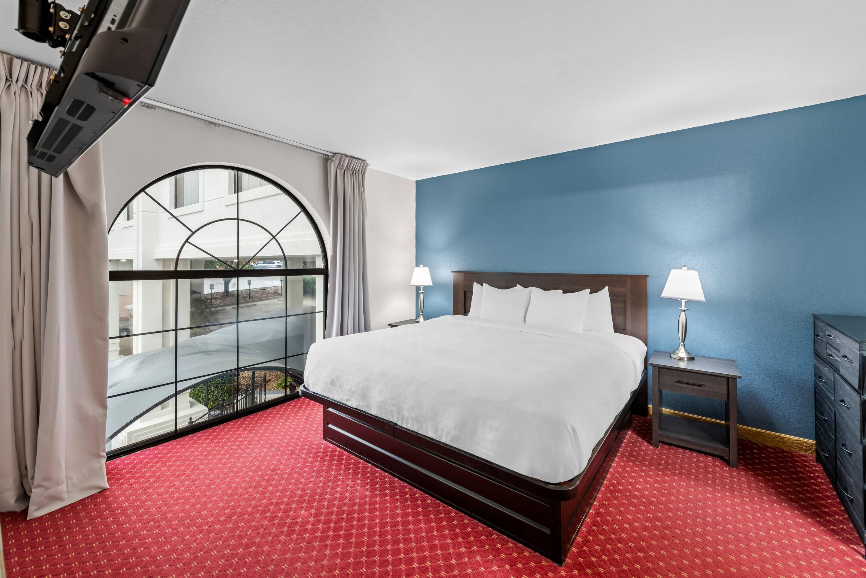 Camera d'albergo con un letto grande, due comodini con lampade, una finestra vista e un tappeto rosso.