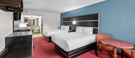 Una habitación de hotel con cama, dos mesitas de noche, televisor, escritorio y silla.