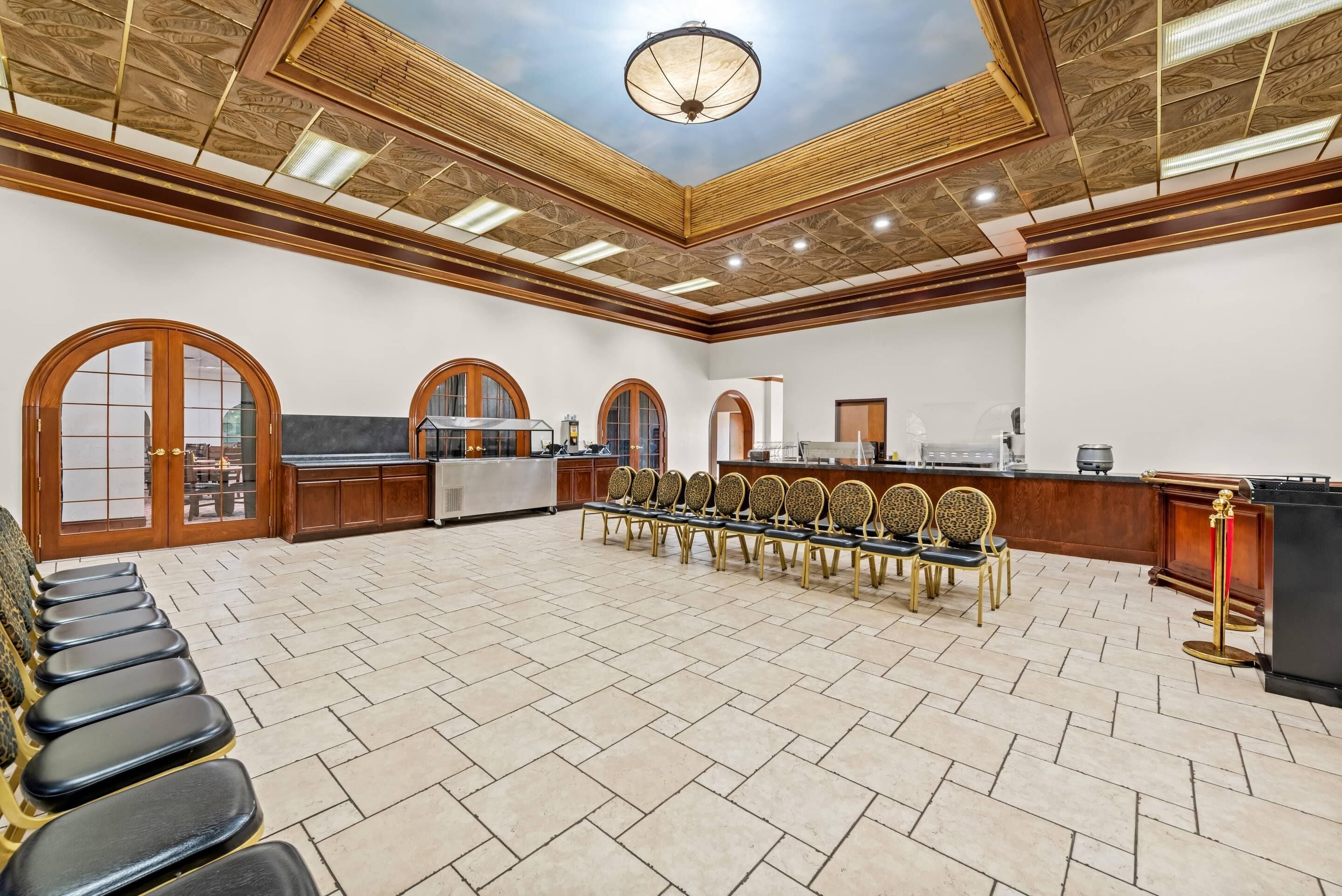 A spacious room with a high ceiling, arched windows, and a long table with chairs.