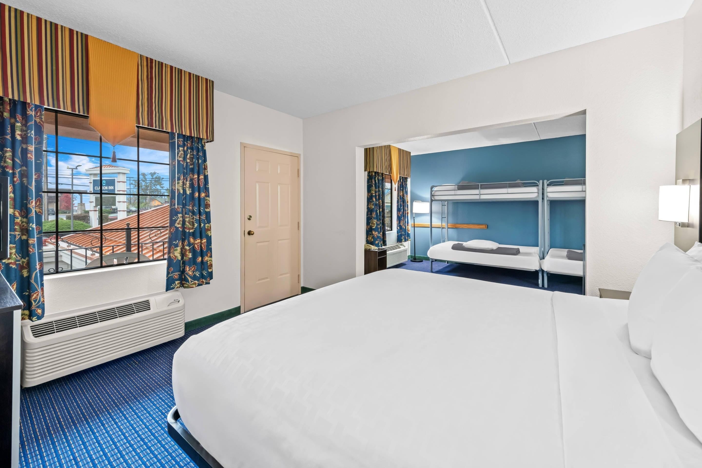 A hotel room with a large bed, a window with curtains, a bunk bed, and a radiator.