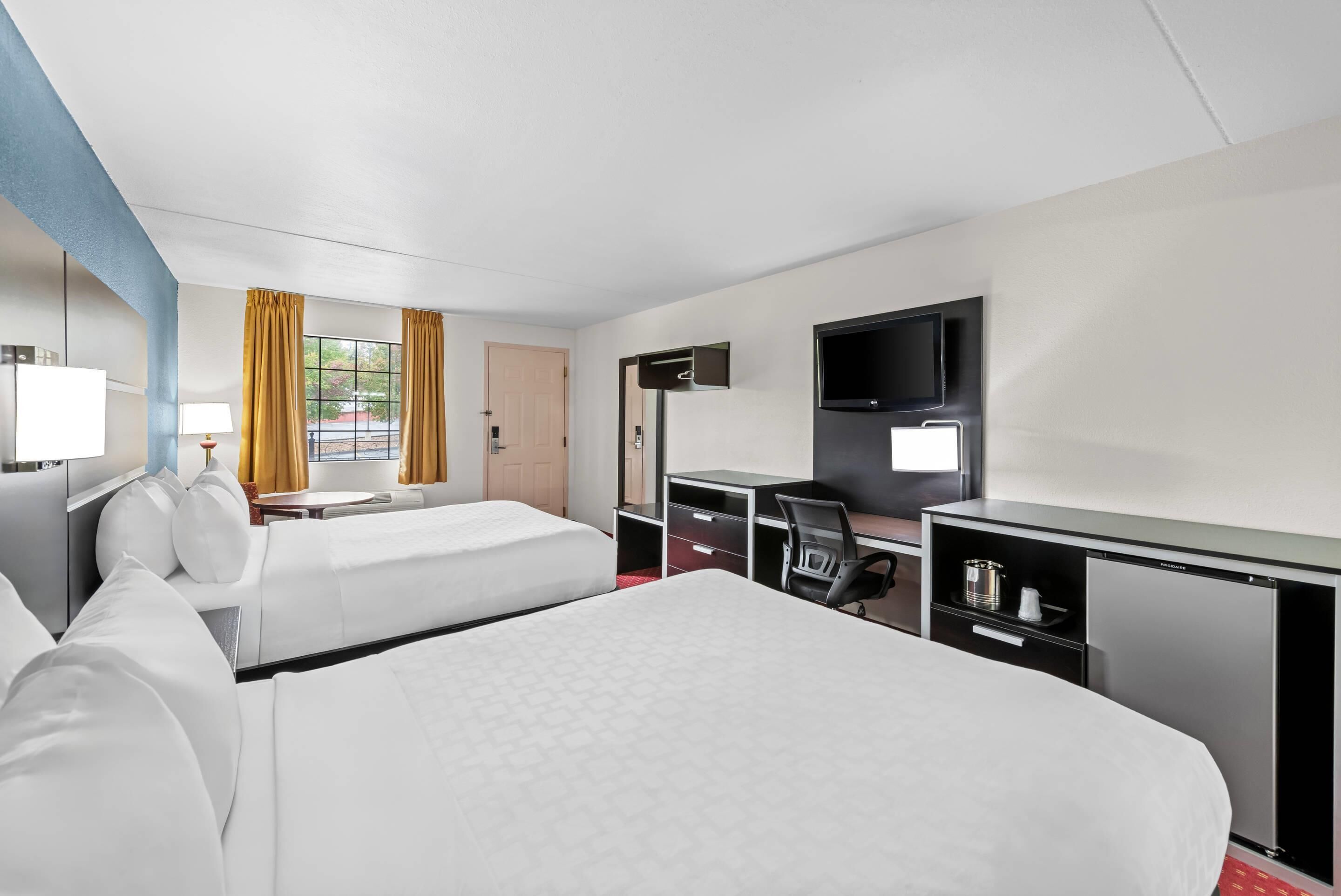 A hotel room with two beds, a desk with a chair, a television, and a window with curtains.