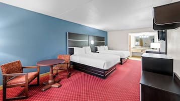 A hotel room with a bed, two chairs, a small table, a TV, and a red carpet.