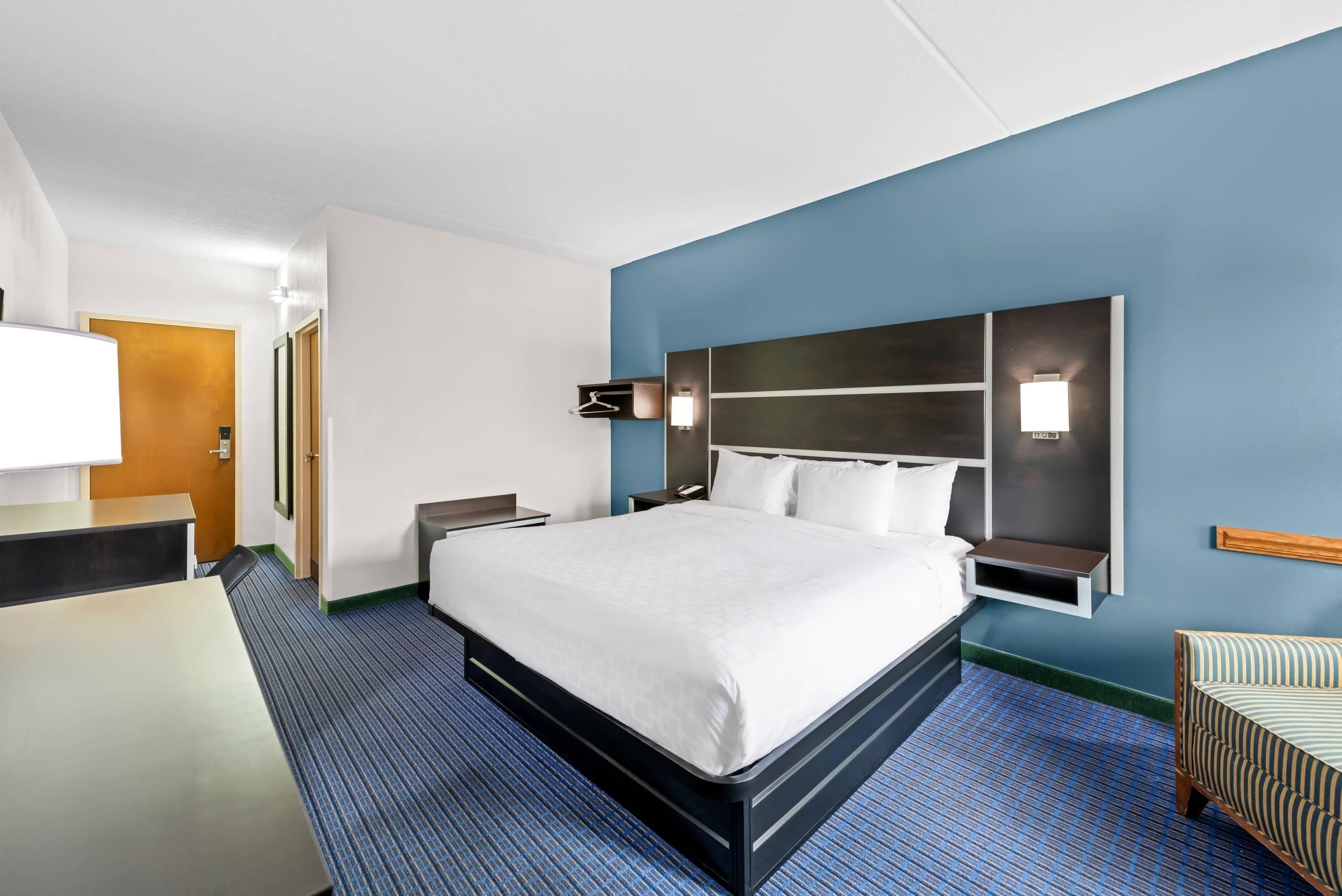 A hotel room with a large bed, a desk, a chair, a nightstand, and a wall-mounted TV.