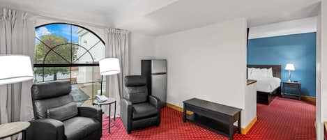 Habitación de hotel con alfombra roja, dos sillones de cuero, una mesita, cama y televisor.