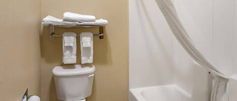 Un baño con inodoro, toallero con toallas dobladas, rollo de papel higiénico y bañera con cortina de ducha.